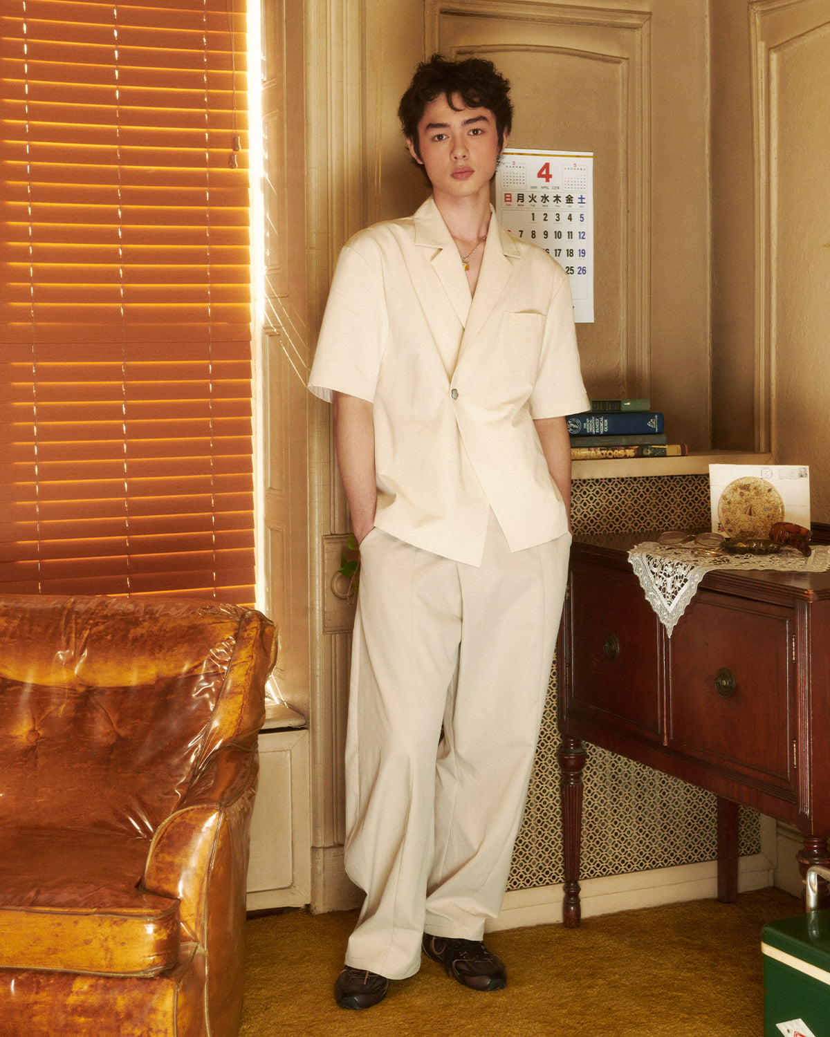 Cream hanbok-inspired short sleeve shirt styled as complete look with cream wide-leg pants, photographed in warm interior setting with vintage furniture, wooden blinds, and calendar, demonstrating coordinated suiting option
