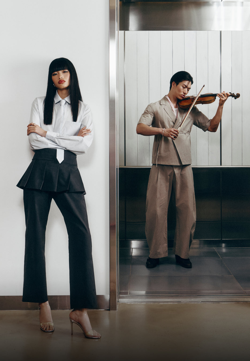 Two people, one in formal attire and the other playing violin, in an elevator setting.