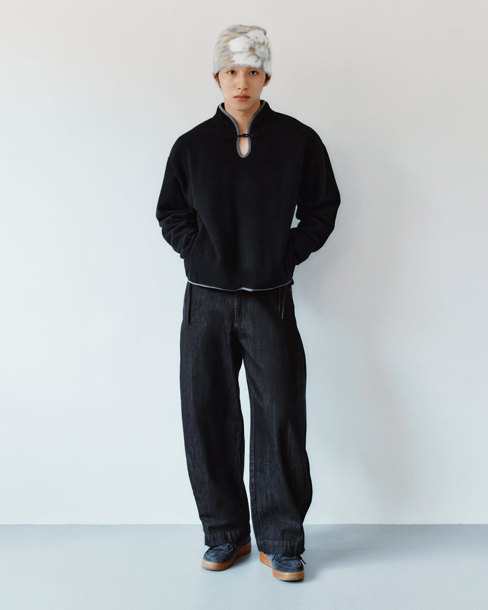A person wearing a black mock-neck sweatshirt with a keyhole detail and BLACK ACCORDION DENIM PANTS in black.