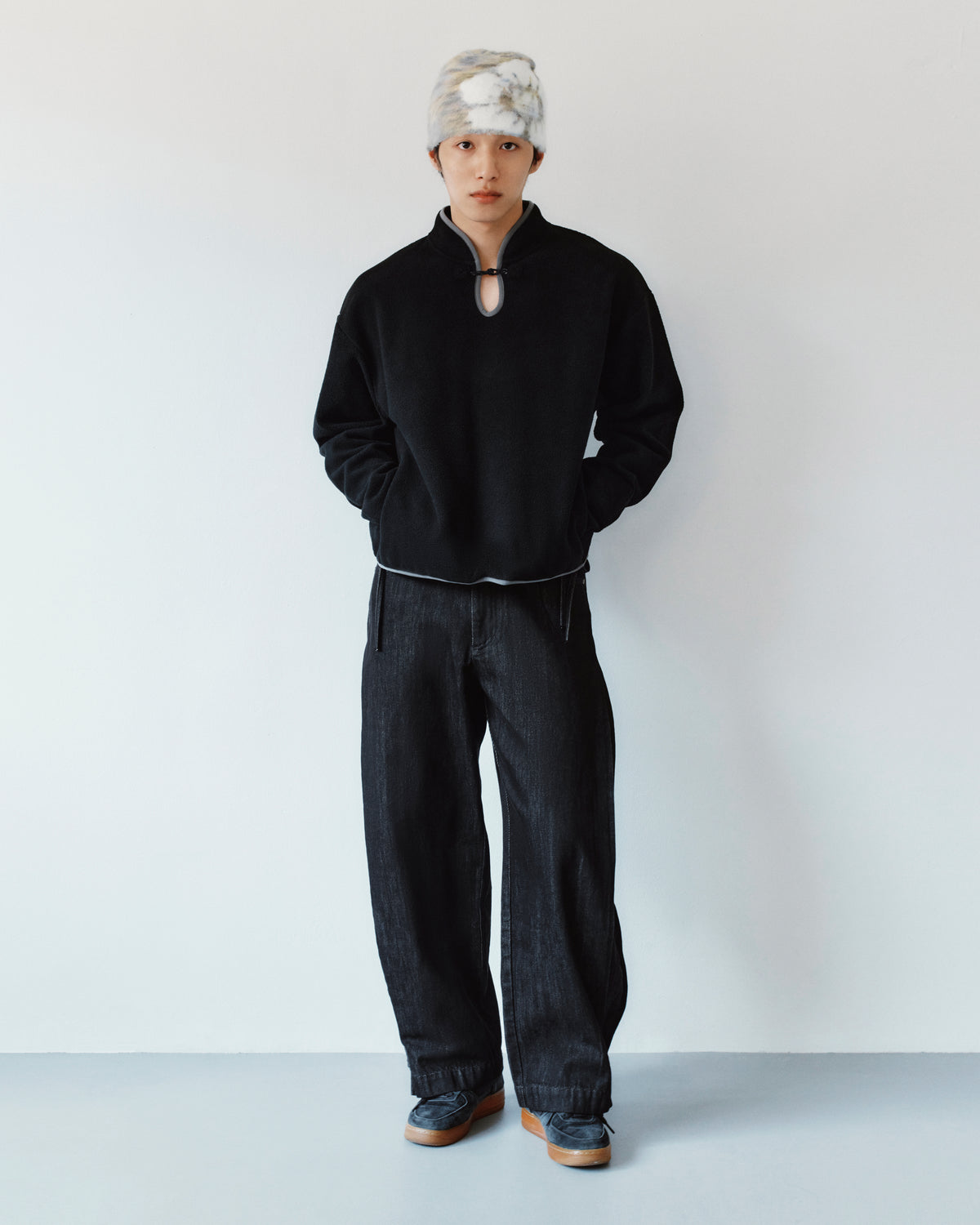 A person wearing a black mock-neck sweatshirt with a keyhole detail and BLACK ACCORDION DENIM PANTS in black.