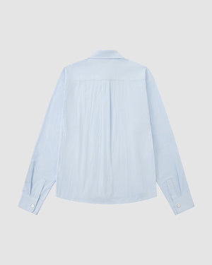 The SKY BLUE TIE GORUM SHIRT by Sundae School is displayed from the back against a white background, showcasing its classic collar, subtle pleats below the yoke, long sleeves, button cuffs, and light blue seersucker cotton fabric.