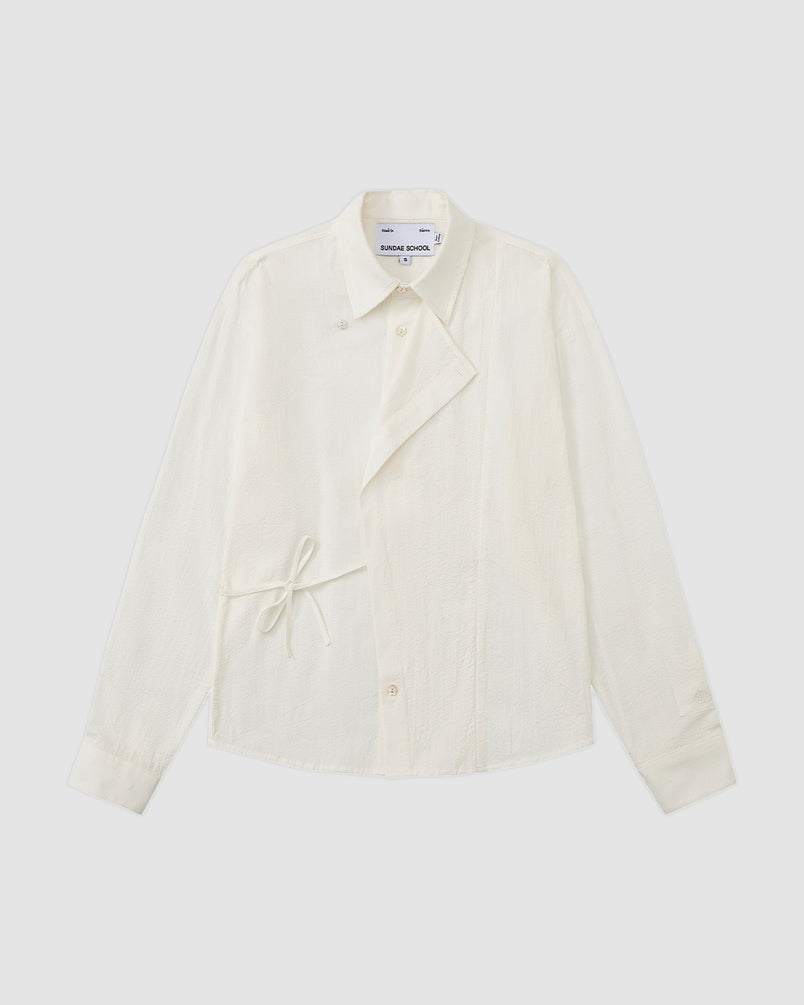 An IVORY TIE GORUM SHIRT by Sundae School, featuring long sleeves, a collar, gorum tie detail, and asymmetrical button closure, laid flat on a light background.