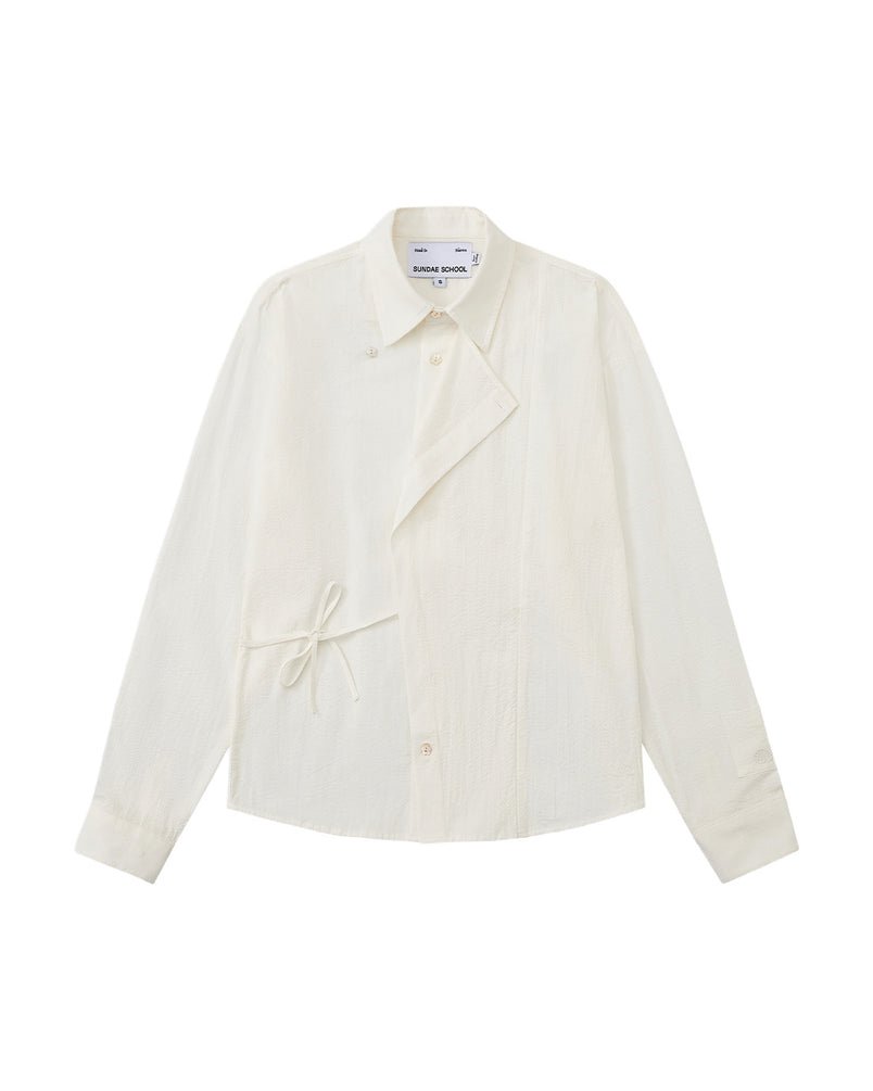 A front flat-lay view of an off-white long-sleeve button-up shirt crafted from textured crinkle fabric. It features an asymmetrical wrap-front construction with a side waist tie, a pointed collar, and flower-shaped button details.