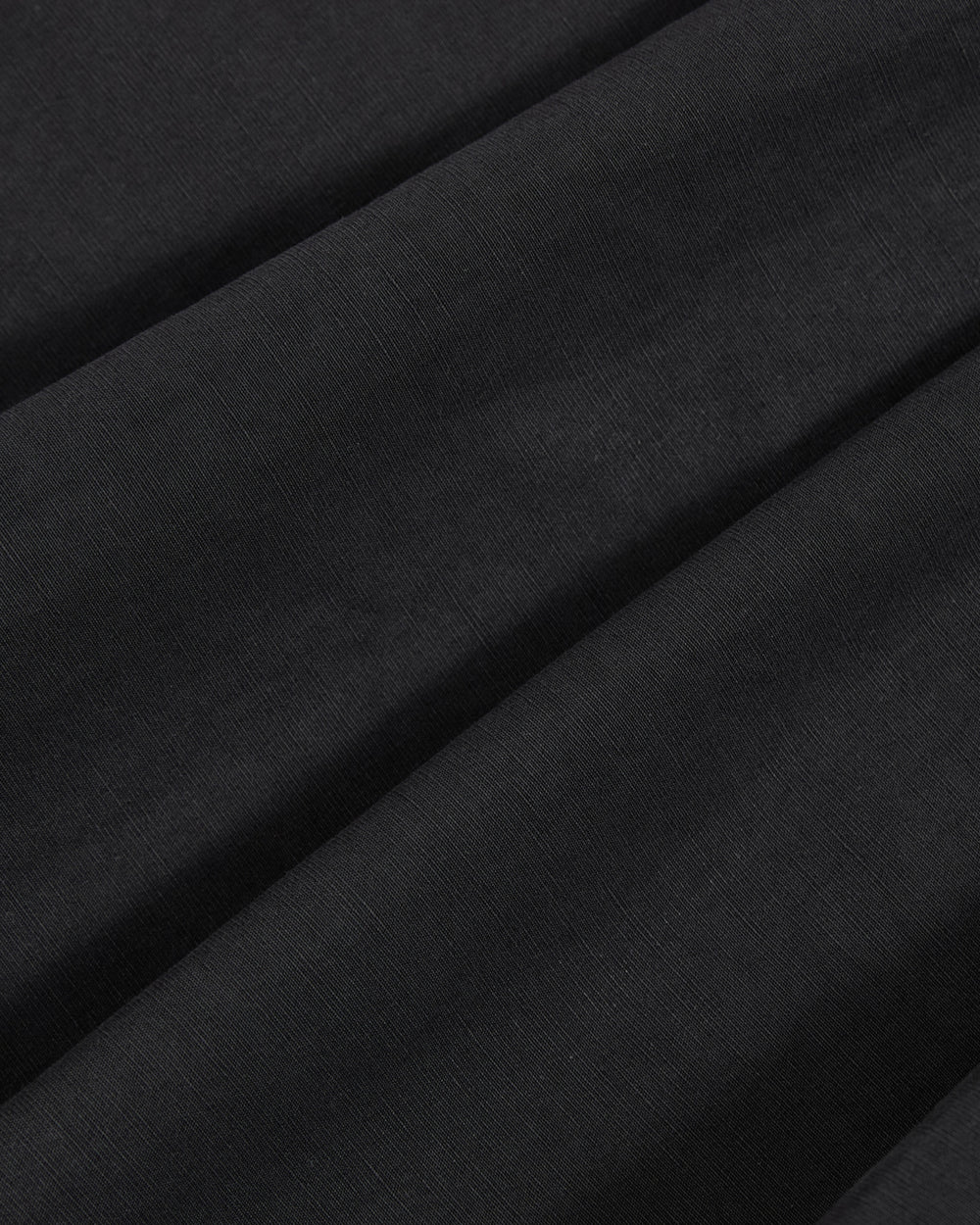 Close-up of smooth, black fabric with subtle diagonal folds and a soft texture, showcasing the weave and drape of the material—featured in Sundae School’s ASYMMETRIC CHIMA CULOTTE.