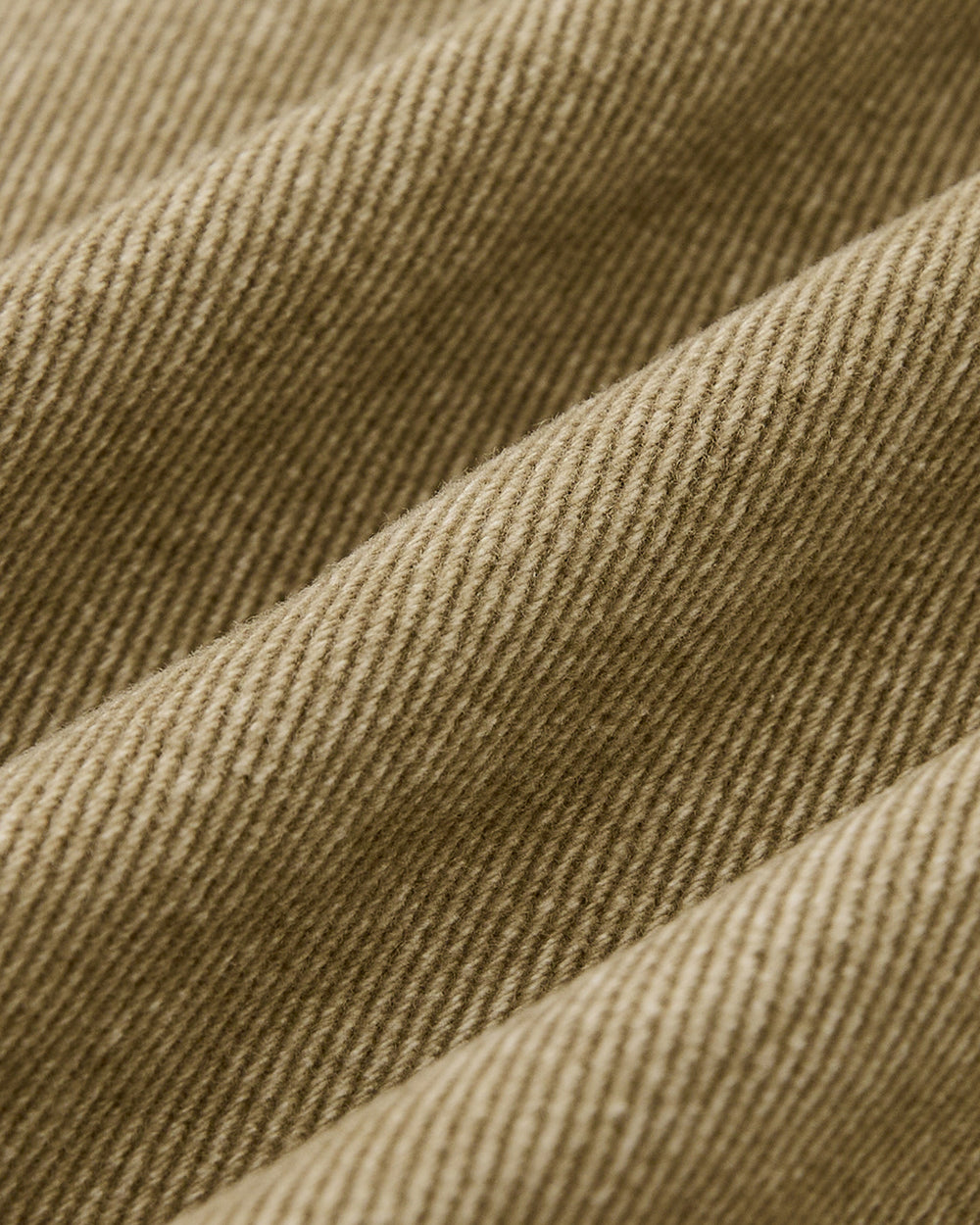 Close-up of light brown corduroy from the Sundae School TAN ASYMMETRIC WORK JACKET, highlighting its textured ridges and diagonal weave with soft lighting that accentuates the jacket's folds and fabric detail.