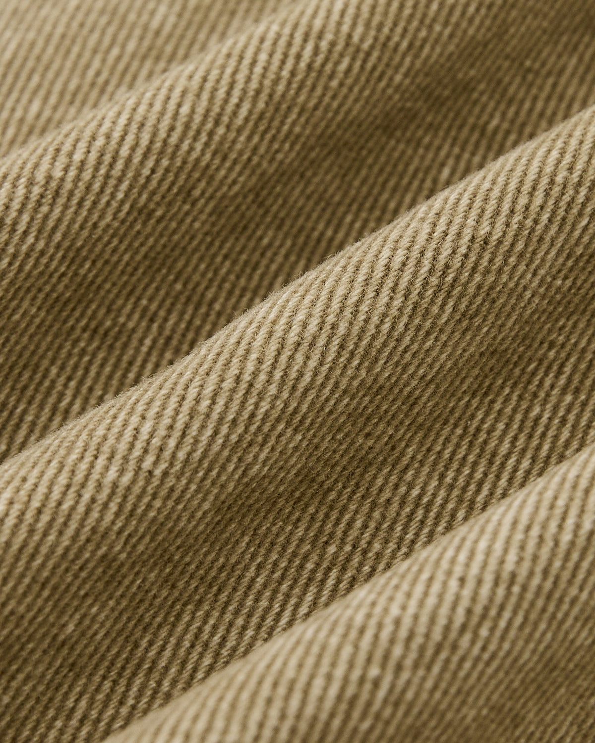 Close-up of light brown corduroy from the Sundae School TAN ASYMMETRIC WORK JACKET, highlighting its textured ridges and diagonal weave with soft lighting that accentuates the jacket's folds and fabric detail.