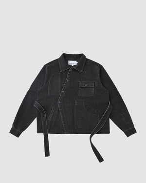 The BLACK ASYMMETRIC WORK JACKET by Sundae School is a black denim unisex piece with white stitching, button closure, long sleeves, pockets, and adjustable side fabric straps. Shown on a plain light gray background.