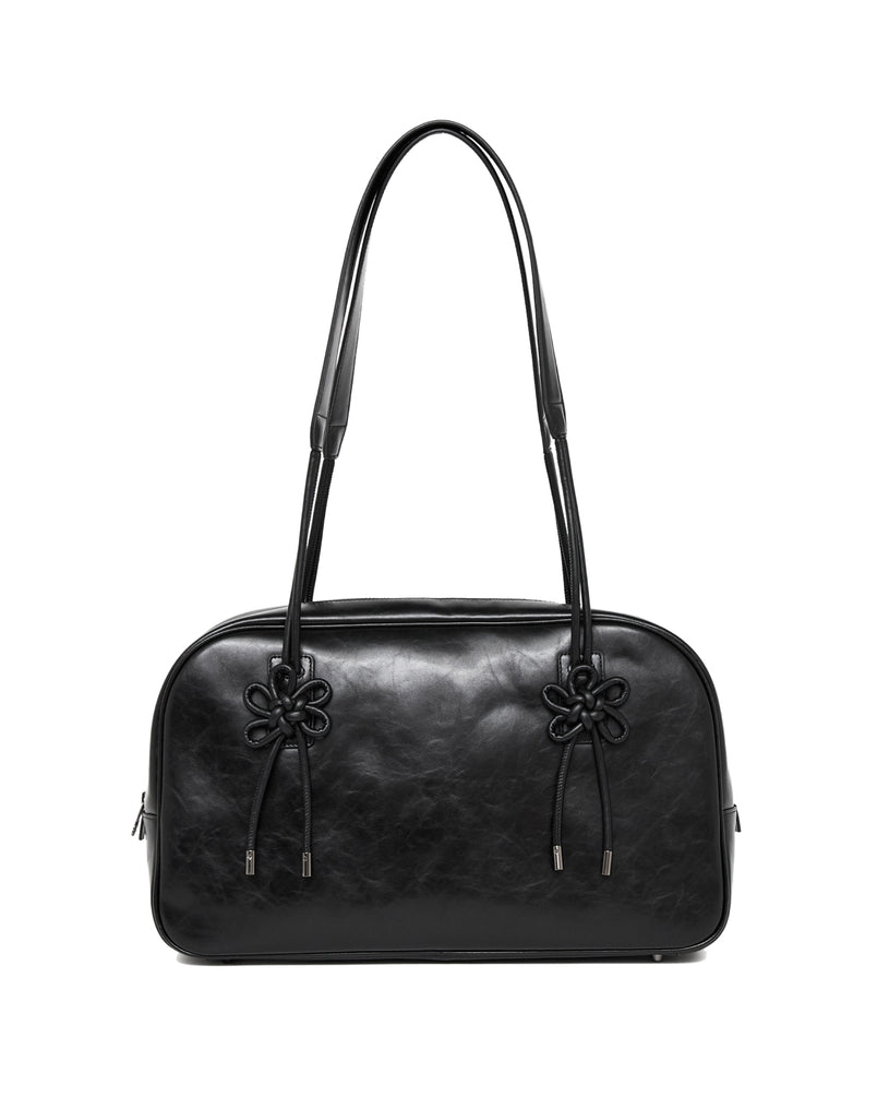 The BLACK AUDREY BOWLING BAG by Sundae School is a black leather handbag featuring two long handles and decorative knots on the front, displayed against a white background.