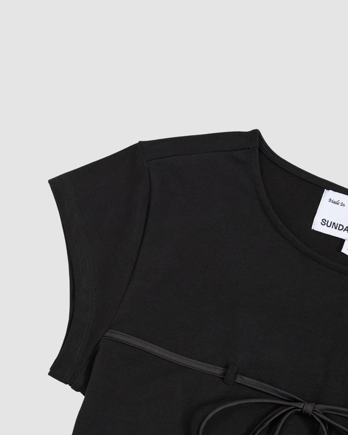 Close-up of the BLACK TIE GORUM BABY TEE by Sundae School, a black, form-fitting women's top with short sleeves, round neckline, and thin tied belt below the chest; two white tags visible inside the collar.