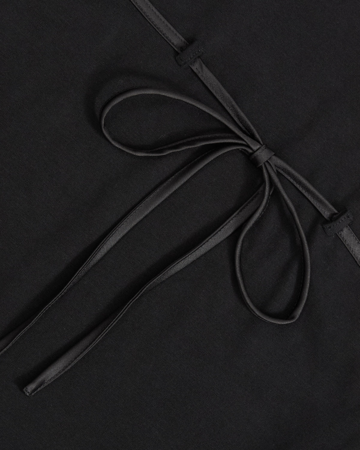 Close-up of the BLACK TIE GORUM BABY TEE by Sundae School, a black cotton tee featuring a neatly tied black ribbon bow at the center, laid flat on soft fabric.