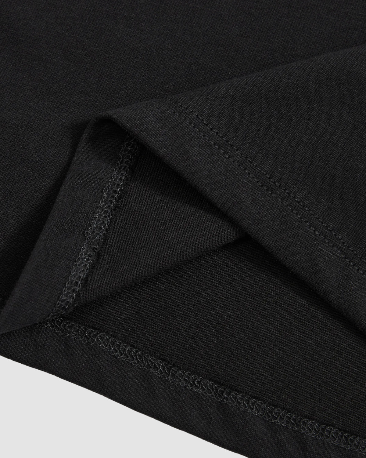 Close-up of the hem and stitching on Sundae School's BLACK TIE GORUM BABY TEE, highlighting its overlapping edges and detailed seam work against a light background.
