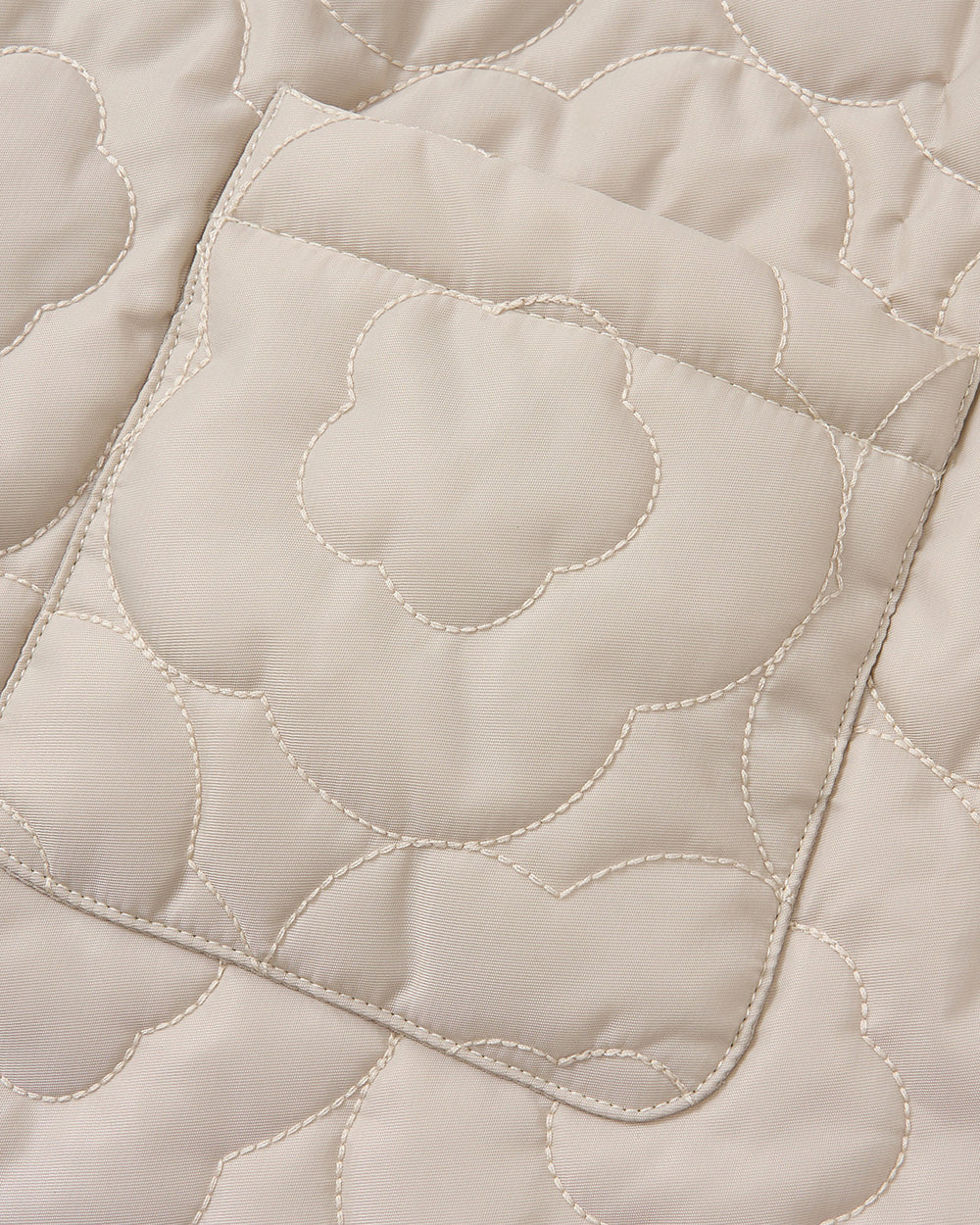 Close-up of the SILVER PINK BAEJA VEST / BAG by Sundae School, showcasing beige quilted fabric adorned with a stitched floral pattern and a rectangular pocket with rounded corners. The contrasting light stitching highlights the meticulous craftsmanship inspired by traditional Korean baeja vests, set against smooth fabric.