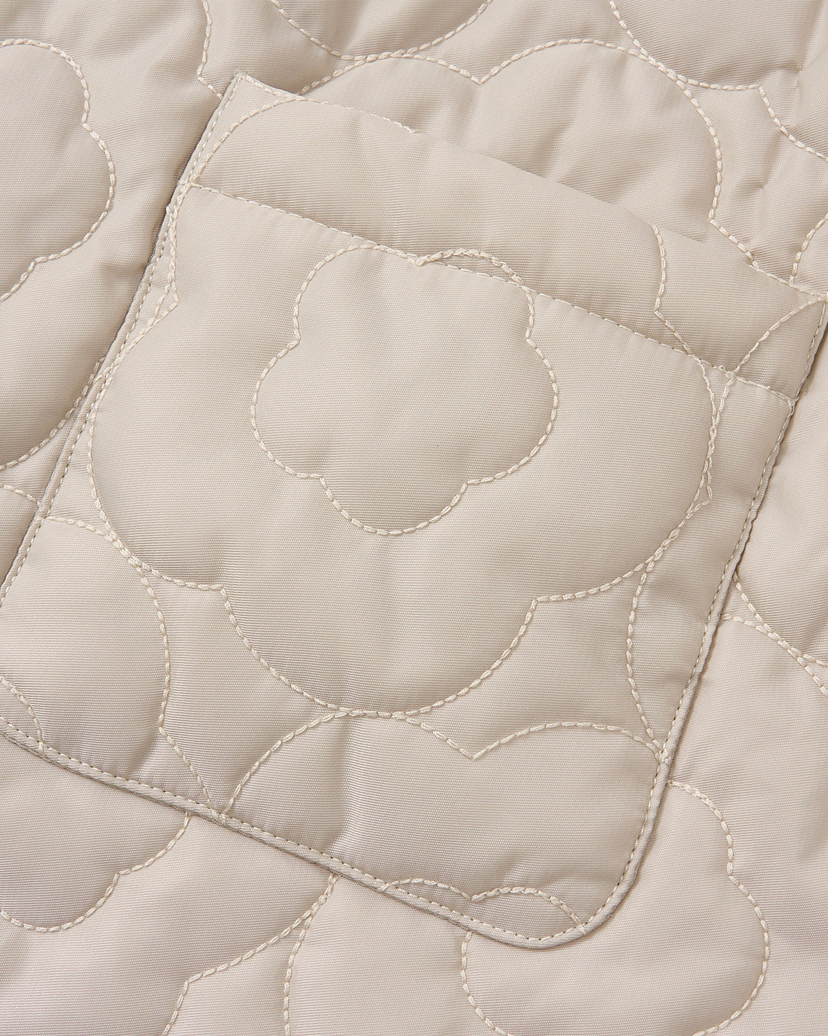 Close-up of the SILVER PINK BAEJA VEST / BAG by Sundae School, showcasing beige quilted fabric adorned with a stitched floral pattern and a rectangular pocket with rounded corners. The contrasting light stitching highlights the meticulous craftsmanship inspired by traditional Korean baeja vests, set against smooth fabric.