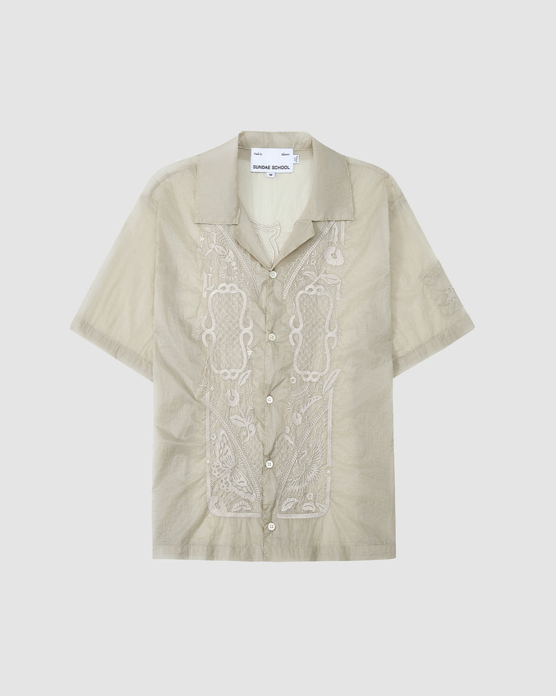 The BARONG SHIRT by Sundae School is a light beige, short-sleeve button-up with a collar and white embroidery on the front. Inspired by the Barong Tagalog, it offers a relaxed fit and casual style.