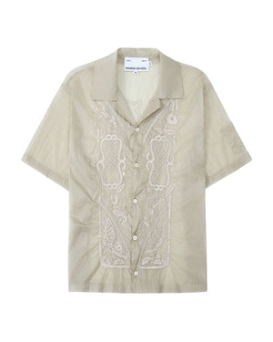 The BARONG SHIRT by Sundae School is a light beige short-sleeve button-up featuring intricate embroidery on the front, a camp collar, and design details inspired by the classic Filipino Barong Tagalog silhouette. This relaxed-fit shirt includes a visible Sundae School label inside the collar and subtle references to traditional craftsmanship.