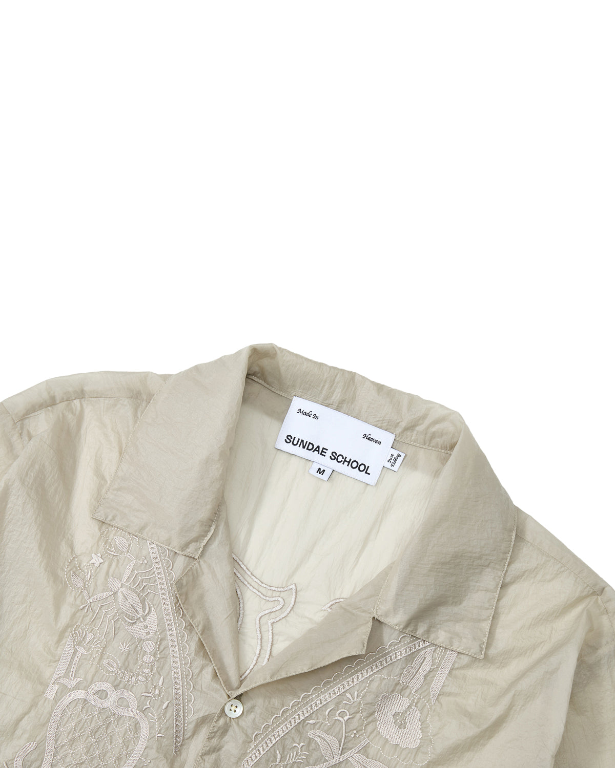 The BARONG SHIRT by Sundae School is a light beige, partially folded collared shirt featuring white embroidery and translucent nylon fabric that evokes the classic Filipino Barong Tagalog silhouette. The inner tag displays SUNDAE SCHOOL, and the shirt is size M.