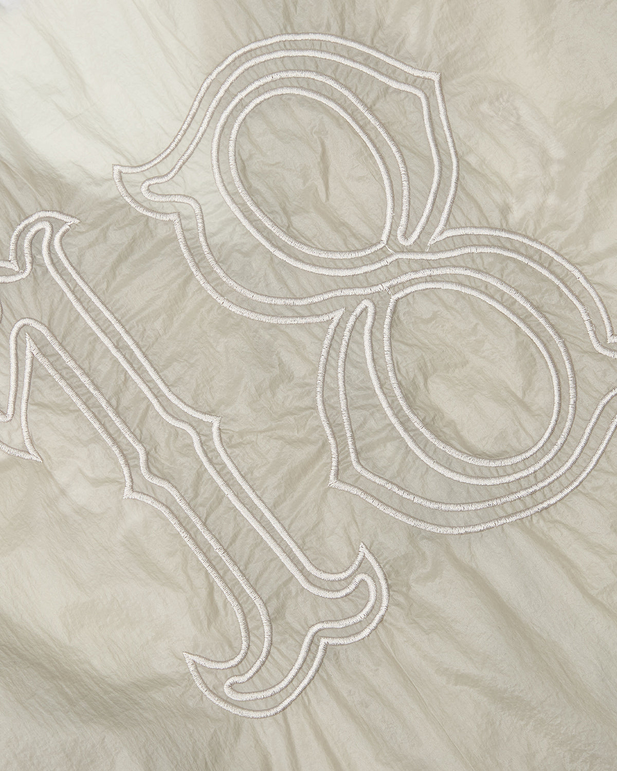 Close-up of the BARONG SHIRT by Sundae School, featuring beige fabric with an embroidered outline of the number 198 in a decorative font. The slightly wrinkled texture and intricate detailing are reminiscent of the refined craftsmanship and subtle elegance found in traditional Filipino Barong Tagalog silhouettes.
