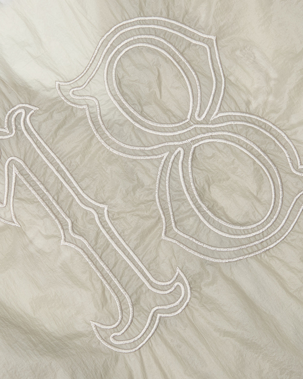 Close-up of the BARONG SHIRT by Sundae School, featuring beige fabric with an embroidered outline of the number 198 in a decorative font. The slightly wrinkled texture and intricate detailing are reminiscent of the refined craftsmanship and subtle elegance found in traditional Filipino Barong Tagalog silhouettes.