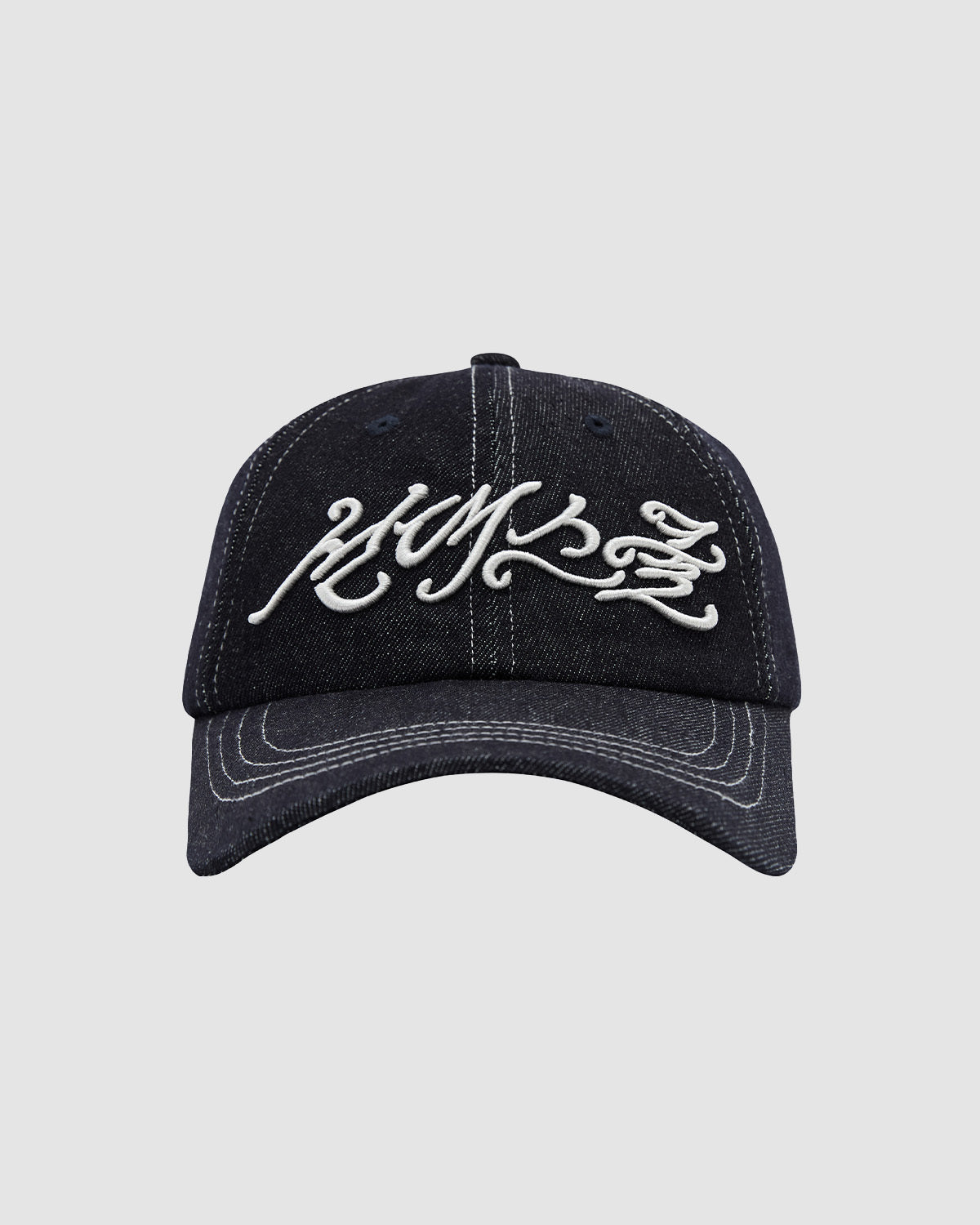 The INDIGO DAENGGI CAP by Sundae School is a black denim 6-panel cap with adjustable fit, white stylized script embroidery on the front, and crisp visible white stitching along the brim and panels.
