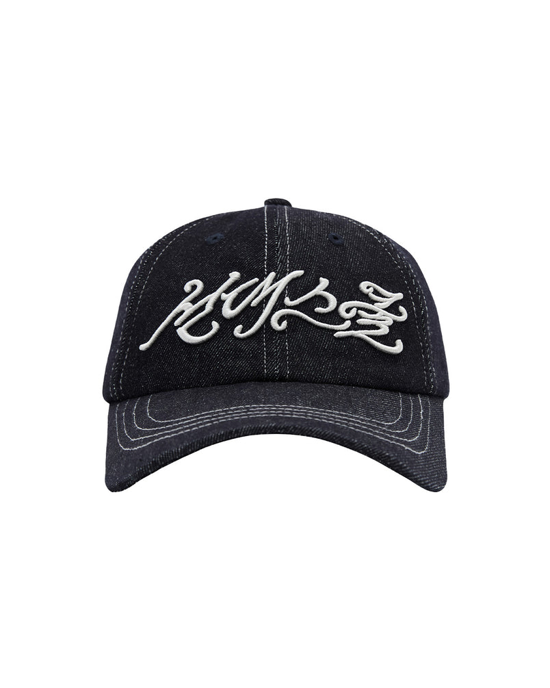 Introducing the INDIGO DAENGGI CAP by Sundae School: a black denim baseball cap adorned with white embroidered graffiti-style text on the front and an embroidered Hangeul logo. Designed for comfort with an adjustable fit, this cap is complemented by distinctive white stitching along the brim and panels.