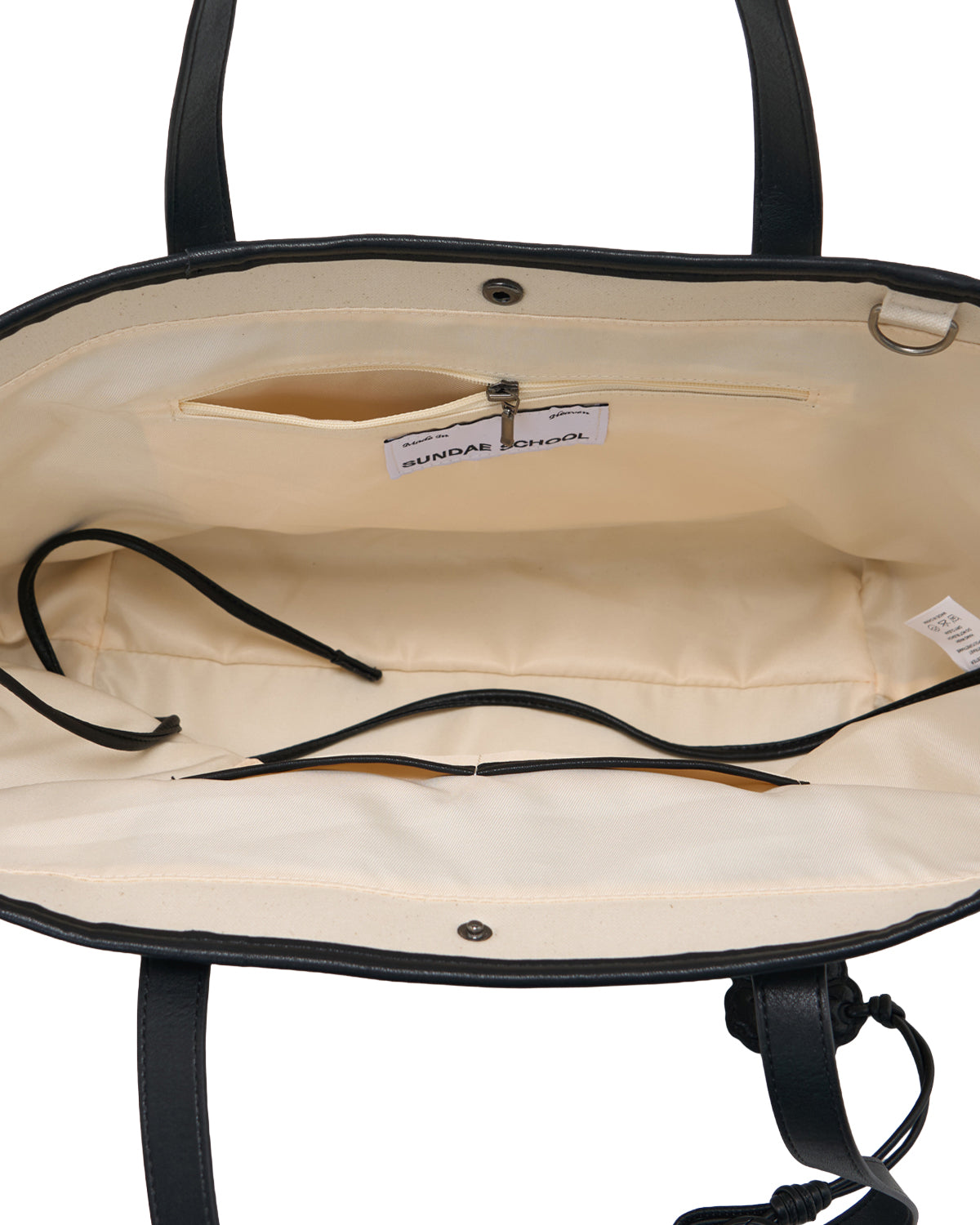 Discover the IVORY BOJAGI TIE TOTE BAG by Sundae School—an open tote featuring a cream interior, vegan leather trim, zippered pocket, small label, fabric tag, and black drawstring-style inserts. With two handles and a magnetic snap closure, this versatile foldable canvas bag is perfect for everyday use.