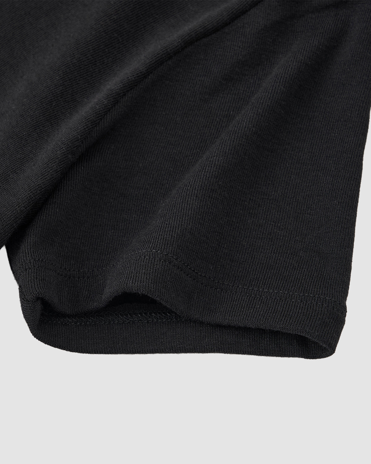 Close-up of the hem and sleeve of the Sundae School CINDY POLO DRESS in black, highlighting its knit texture and stitching—ideal for layering under a convertible wrap apron—set against a light gray background.
