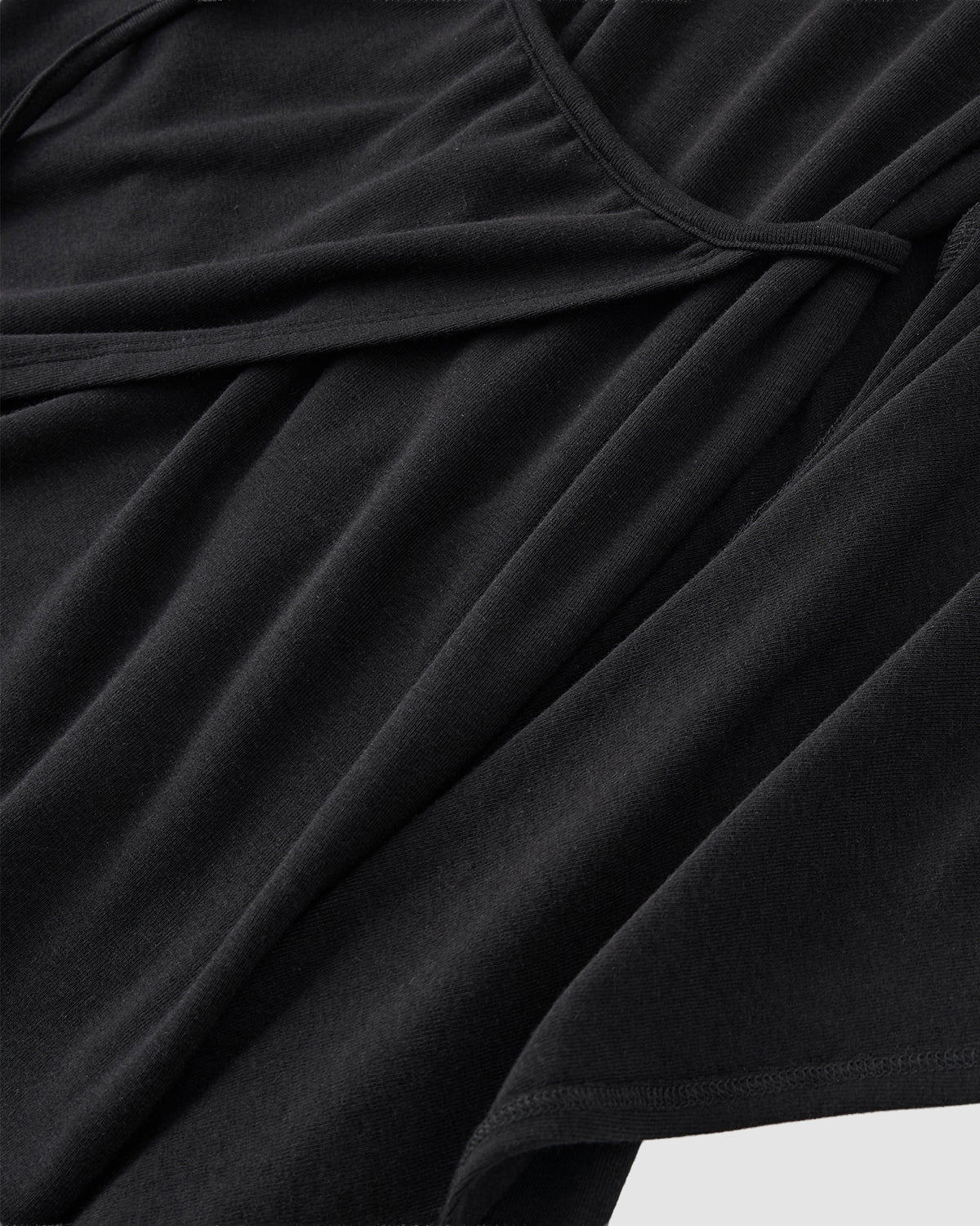 Close-up of the CINDY POLO DRESS by Sundae School, a black wrap-style garment featuring overlapping layers, soft smooth fabric, and a fitted midi silhouette that elegantly drapes with its lightweight material.