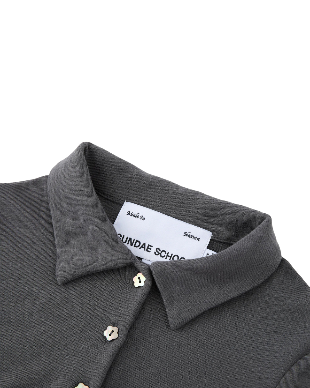 Close-up of the DARK GREY CINDY POLO DRESS by Sundae School, featuring a crisp gray collar, white buttons, and an inside label bearing the brand name. The dress is neatly folded to highlight the collar and part of the button placket—evoking the refined structure typical of a fitted midi silhouette.