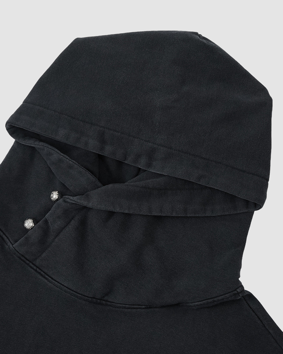 A close-up of the Sundae School FADE BLACK COCOON HOODIE, a limited edition black sweatshirt with an oversized hood, upper shoulder detailing, and two silver snap buttons at the neckline, shown on a light gray background.