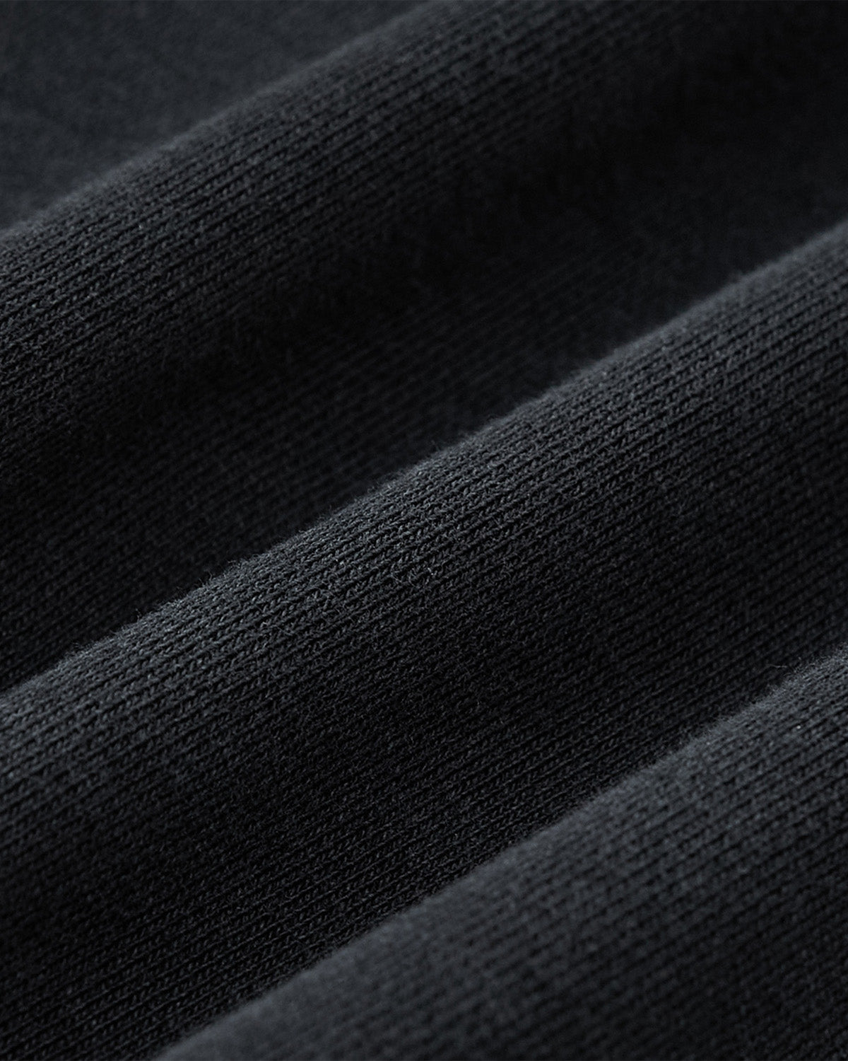 Close-up of the FADE BLACK COCOON HOODIE by Sundae School, highlighting its black ribbed fabric with diagonal folds and soft, smooth knit—ideal for cocoon-core styles.