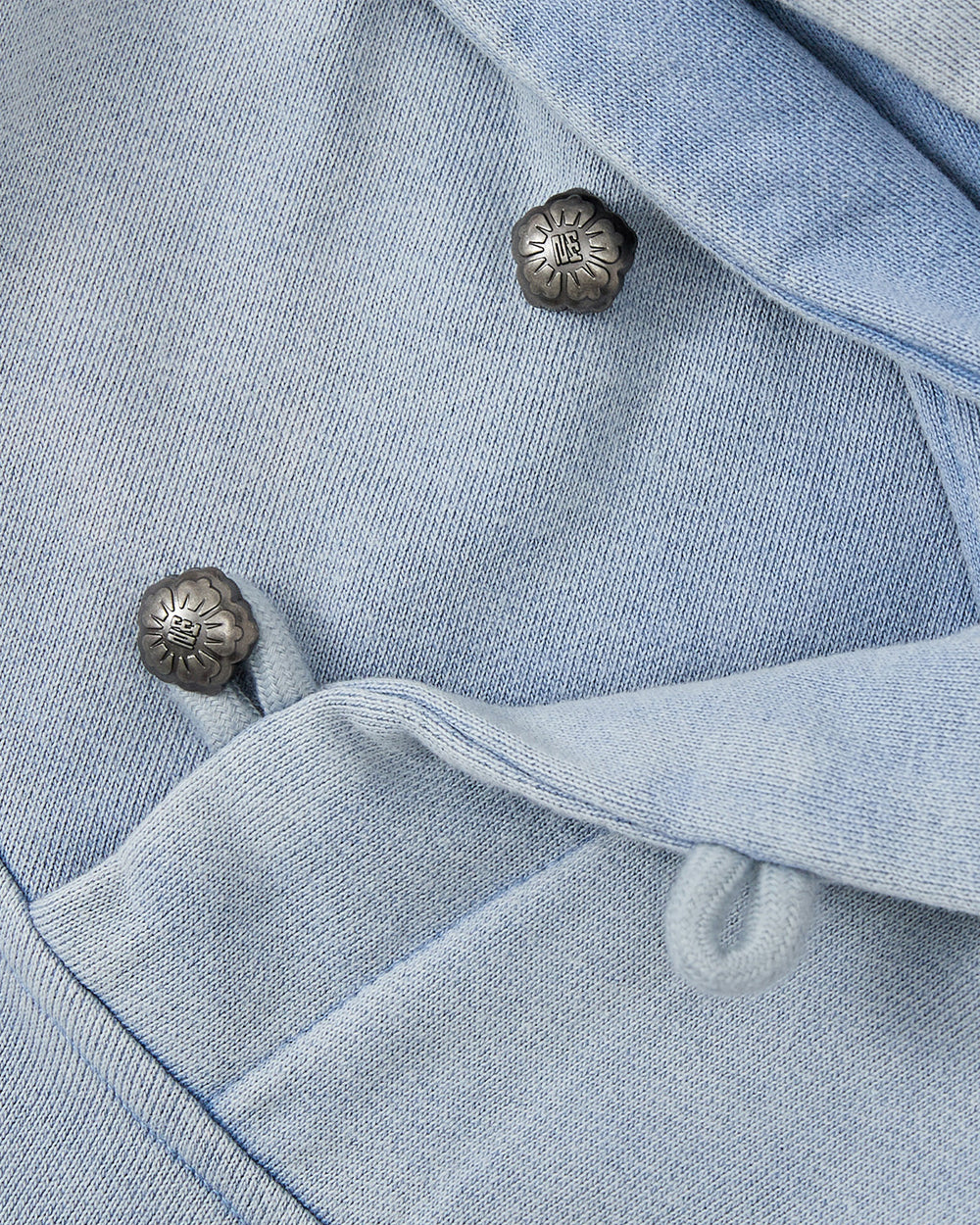 Close-up of SKY BLUE COCOON HOODIE by Sundae School, featuring soft light blue fabric with metal floral buttons and looped fabric fasteners, highlighting its winged silhouette and peret sleeves.