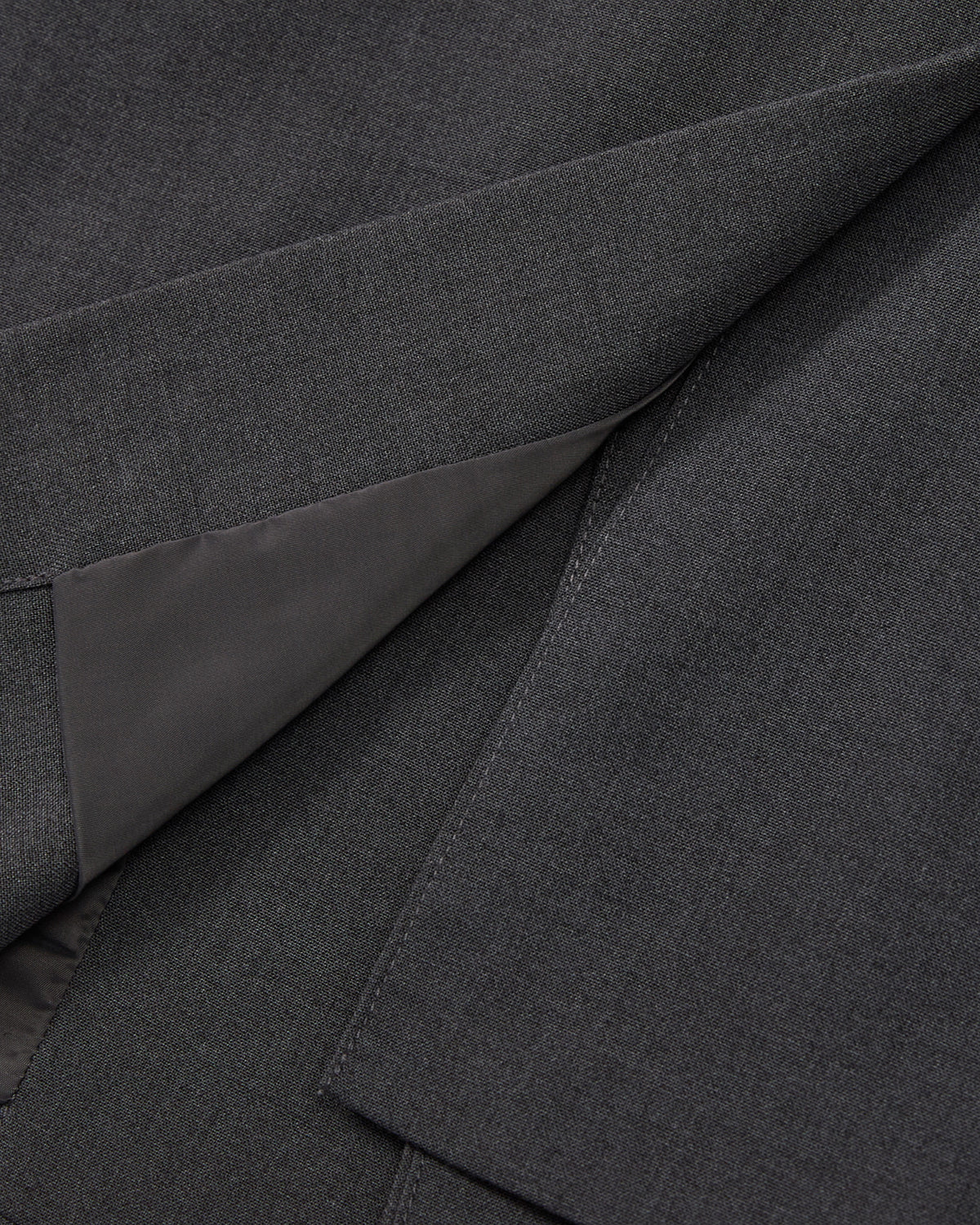 Close-up view of dark gray fabric with smooth lining, showing the folded seam and texture details on the COLLARLESS TIE BLAZER by Sundae School.