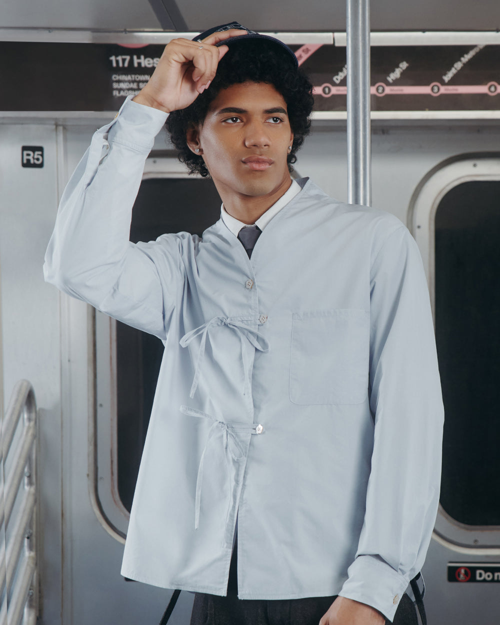 A young man wearing the Sundae School DART COLLAR SHIRT stands in a subway car, holding onto his hat. A subway map and seats are visible in the background.