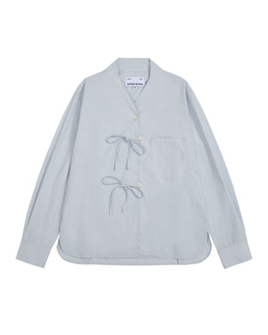 The DART COLLAR SHIRT by Sundae School is a light blue long-sleeve shirt crafted from a soft cotton-nylon blend, featuring two front tie closures, a single chest pocket, and a collarless neckline. Inspired by the relaxed silhouette of a shawl collar shirt, this men’s button-down is displayed flat against a white background.