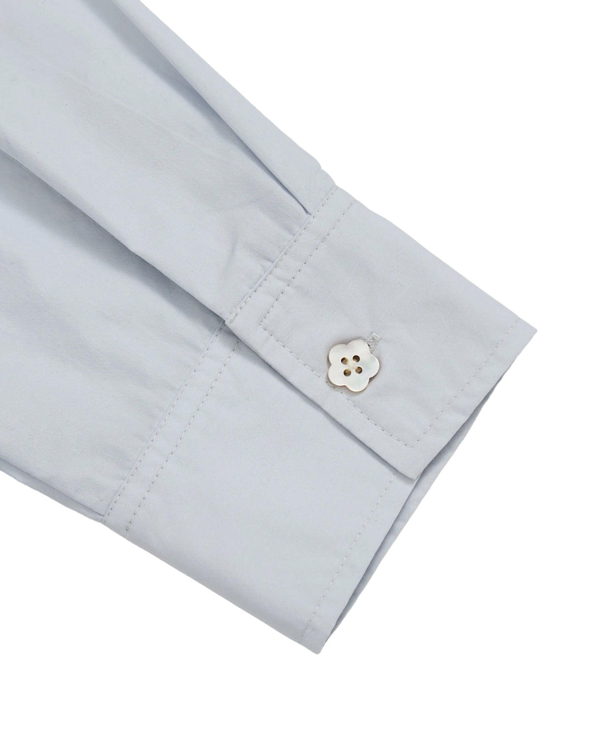 A close-up of the sleeve cuff of the Sundae School DART COLLAR SHIRT in light blue, featuring a white, flower-shaped button fastened on soft cotton-nylon blend fabric.