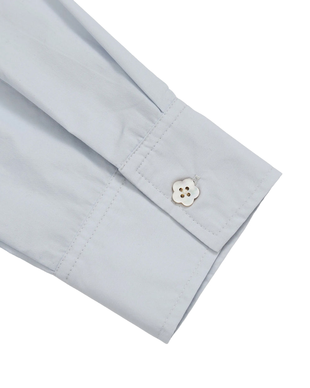 A close-up of the sleeve cuff of the Sundae School DART COLLAR SHIRT in light blue, featuring a white, flower-shaped button fastened on soft cotton-nylon blend fabric.