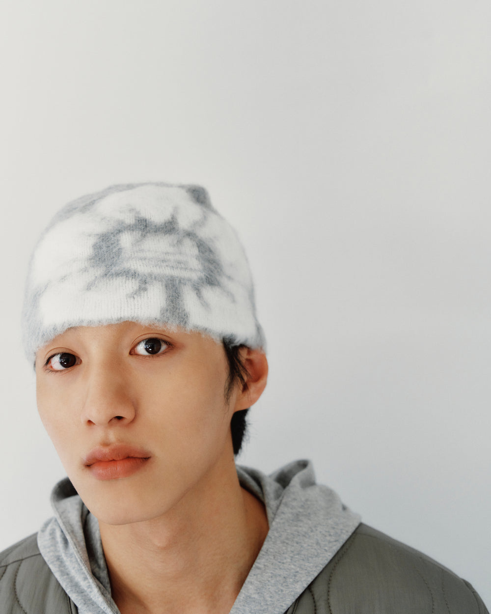 A person wearing a grey and white tie-dye GREY DDUL BEANIE as protective headgear and a grey hoodie.