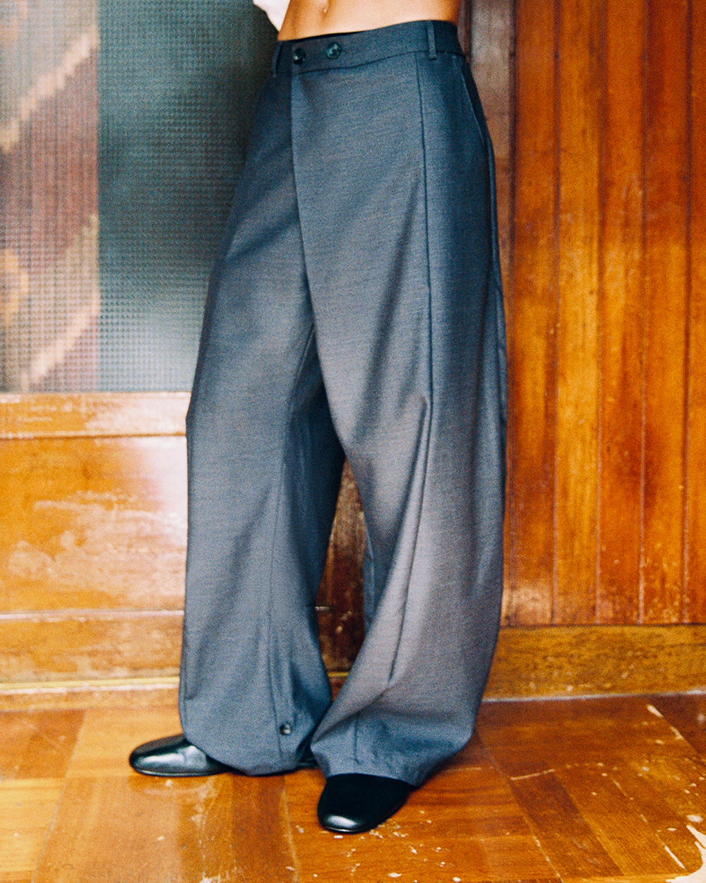Side view of Sundae School CHARCOAL PLEATED HANBOK SLACKS showing the draped wide leg, with black shoes.
