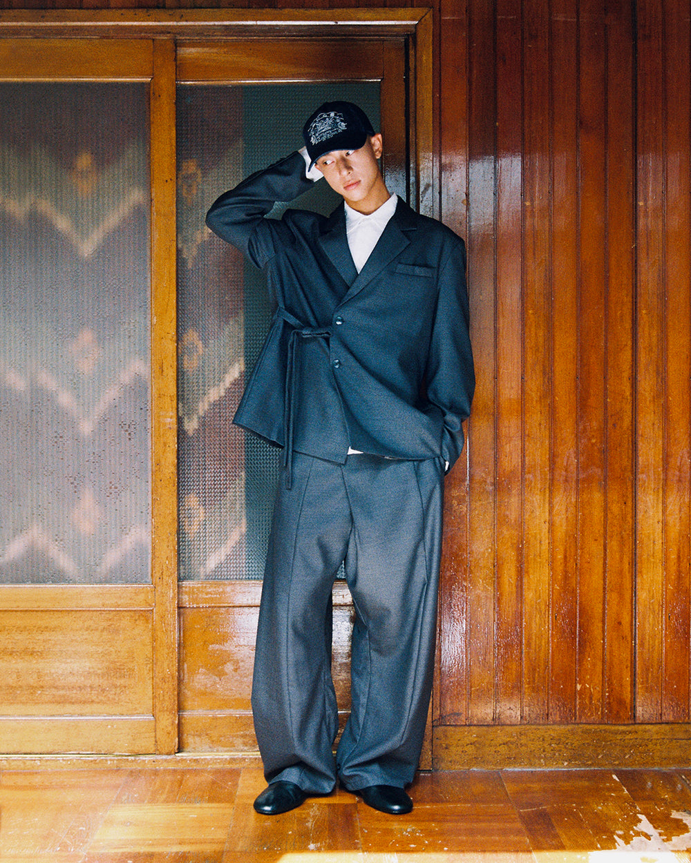 A model adjusts his cap while wearing the Sundae School CHARCOAL DOUBLE DUTY BLAZER and matching CHARCOAL PLEATED HANBOK SLACKS.