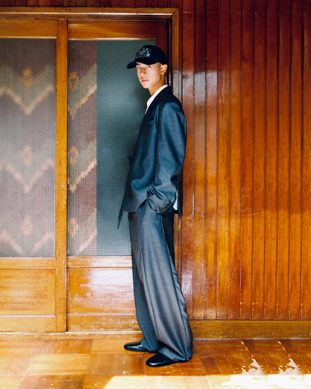 Side profile of a model in the Sundae School CHARCOAL DOUBLE DUTY BLAZER and CHARCOAL PLEATED HANBOK SLACKS, hands in pockets.