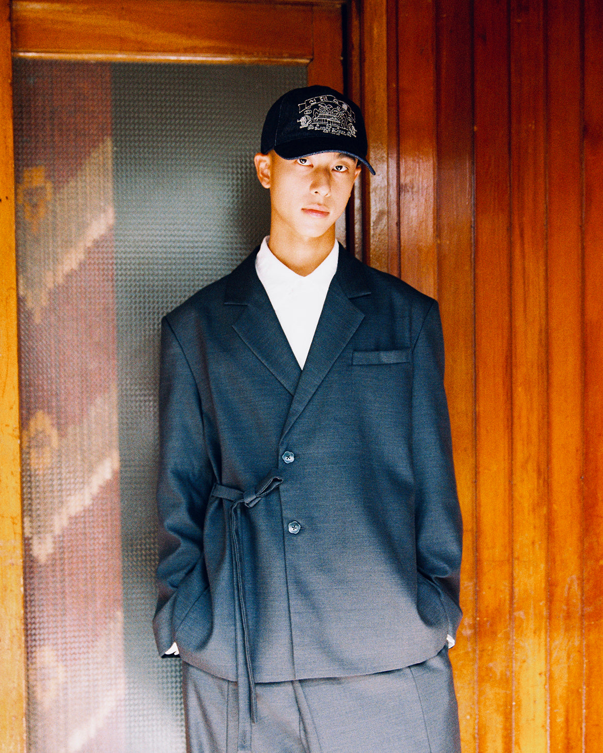 Close-up of a model in the Sundae School CHARCOAL DOUBLE DUTY BLAZER, tied at the waist over a white shirt, with matching charcoal slacks.