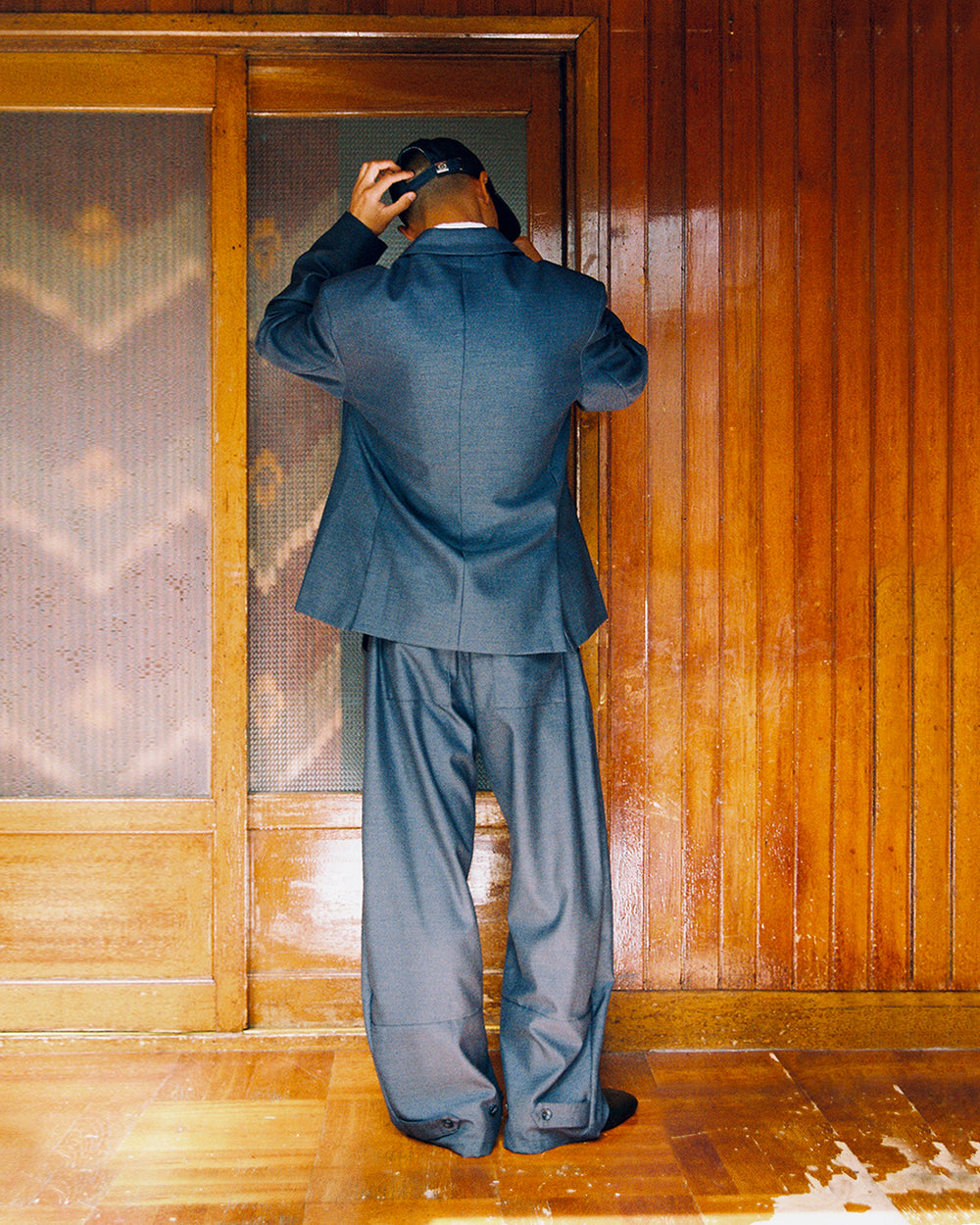 Back view of a model in the Sundae School CHARCOAL DOUBLE DUTY BLAZER and matching CHARCOAL PLEATED HANBOK SLACKS, standing by a wooden door.