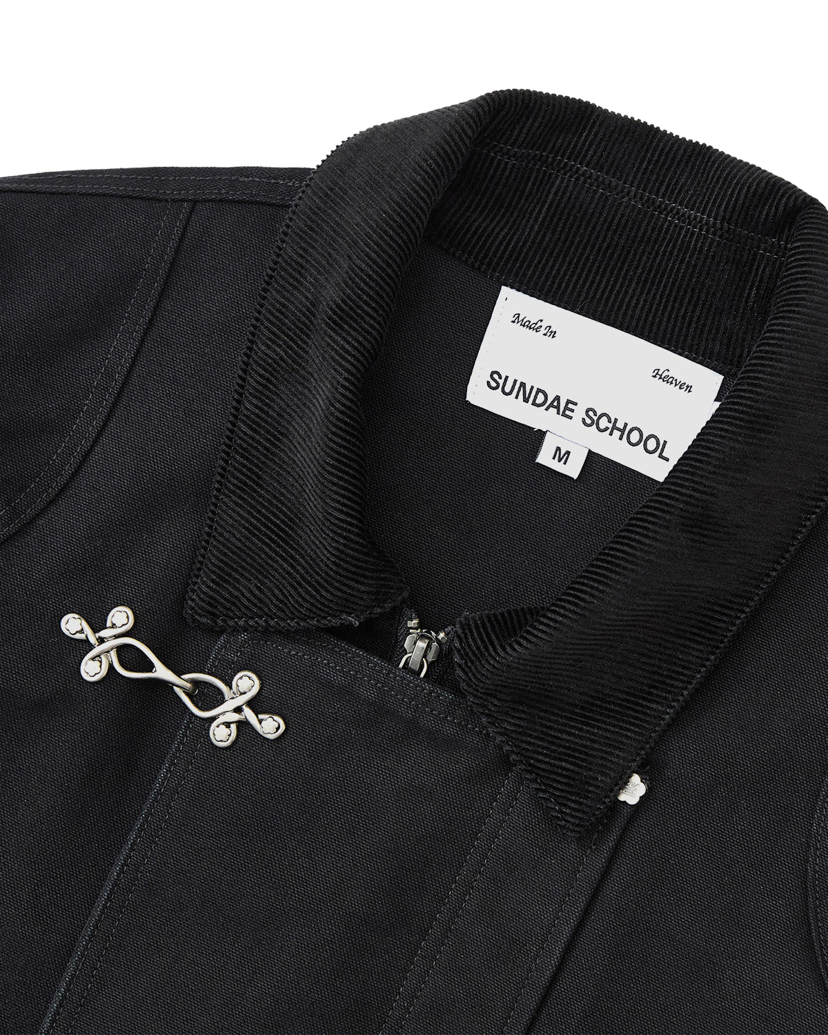 Close-up of the BLACK FIREMAN CLASP JACKET by Sundae School, featuring a ribbed collar, vintage effect, and metal fireman clasp closure. The visible inner label reads SUNDAE SCHOOL M, and the jacket is neatly tailored.