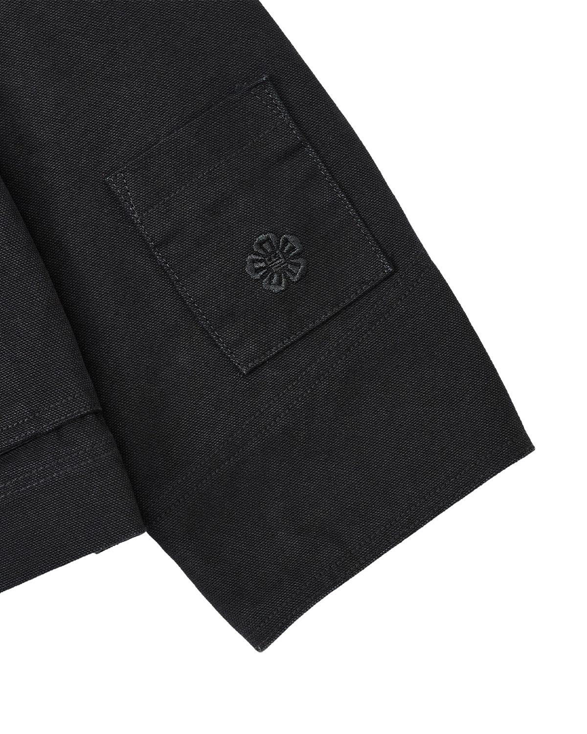 Close-up of the BLACK FIREMAN CLASP JACKET by Sundae School, showcasing a black fabric sleeve with a small patch pocket accented by a delicate embroidered flower motif reminiscent of custom Mochi Floral clasps. The visible texture of the fabric lends a refined vintage touch to the piece.