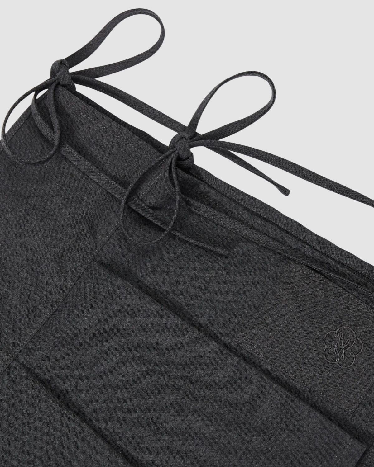 Close-up of Sundae School FLARE SKIRT PANTS in dark grey, featuring two tied fabric bows and a waistband patch with an embroidered flower-like design.