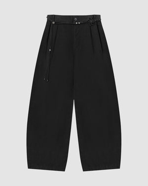 The BLACK FLOWER NORIGAE LINEN TROUSERS by Sundae School feature a wide-leg, balloon silhouette in black cotton linen, pleated at the waist and accented with a norigae belt adorned with bead details. The minimalist design is showcased against a plain light gray background.