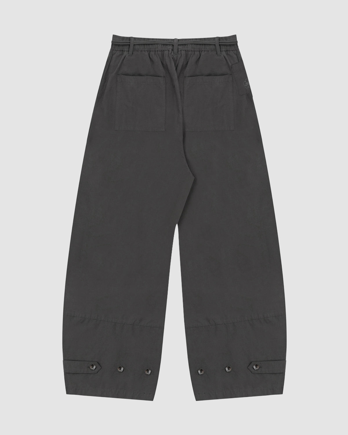 The CHARCOAL FLOWER NORIGAE LINEN TROUSERS by Sundae School are loose-fitting, Korean-inspired balloon pants in black, crafted from a cotton linen blend. They feature an elastic waistband, two large back pockets, and adjustable buttoned straps at the cuffs. The trousers are displayed flat against a plain white background.