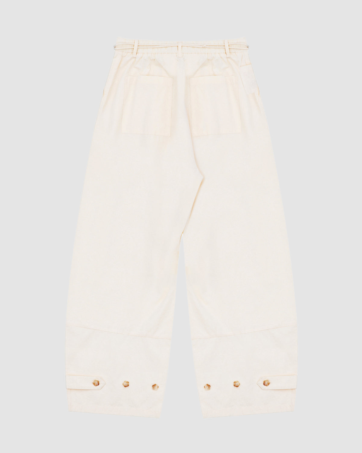 Introducing the IVORY FLOWER NORIGAE LINEN TROUSERS from Sundae School: beige wide-leg pants inspired by Korean heritage, crafted in cotton linen with an elastic waistband, two large back pockets, and adjustable buttoned cuffs at the ankles—beautifully displayed flat on a light background.