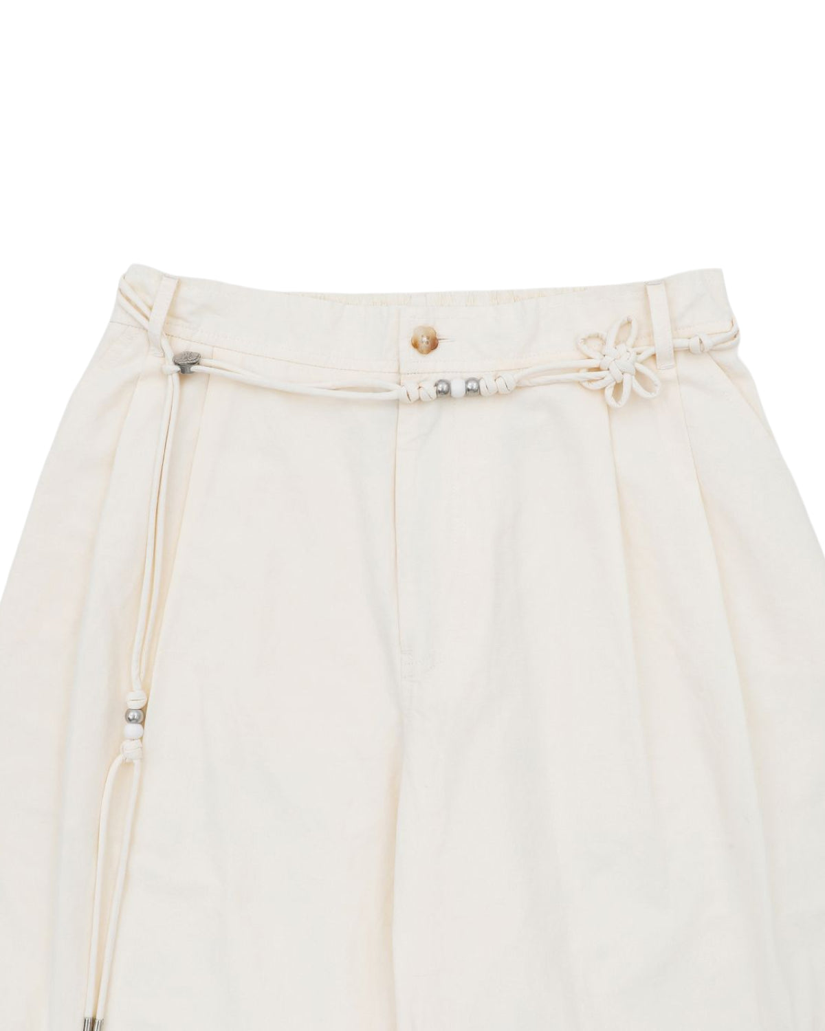 The IVORY FLOWER NORIGAE LINEN TROUSERS by Sundae School are cream-colored, high-waisted cotton linen pants featuring balloon legs and a decorative norigae belt with small metallic beads and a flower-shaped knot detail at the waistband.