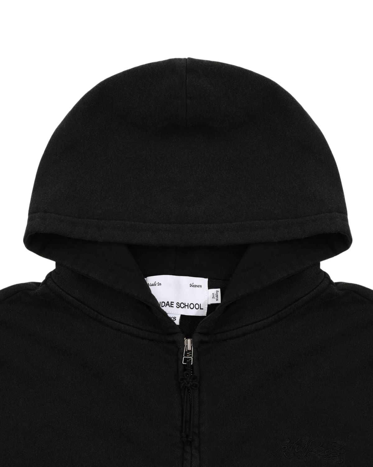 A close-up of the Sundae School BLACK WASH FLOWER KNOT ZIP UP showcases a black cotton zip-up hoodie with visible tags inside the collar, subtle Hangul Sundae School embroidery, and a distinctive Maehwa knot zipper pull.